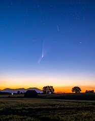 Fototapeta premium Comet streaks across the predawn sky above a rural landscape