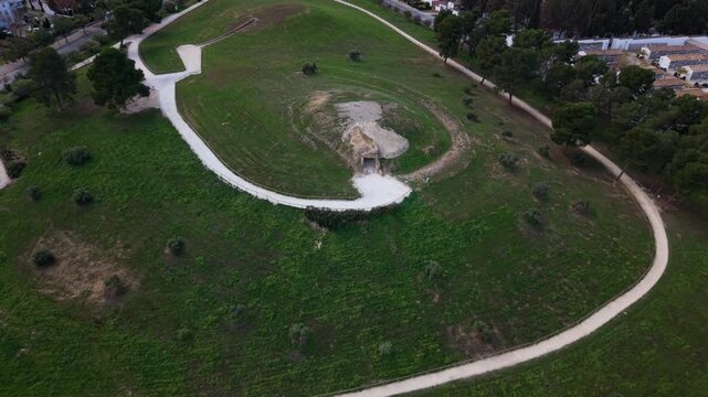 Fast drone fly-away shot from Dolmen de Menga in Antequera, Spain. The camera quickly pulls back from the megalithic burial mound, revealing its surroundings, nearby farmland,