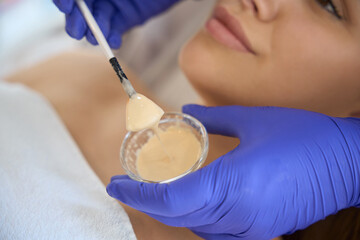Cosmetologist applying chemical peel product on client's face in beauty salon