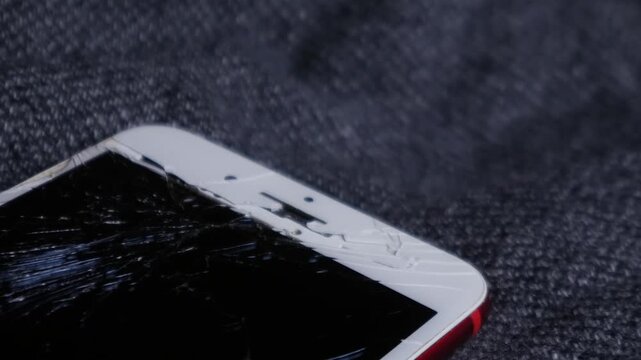 Broken cracked smartphone screen Phone red on dark fabric background, shattered glass display damage concept