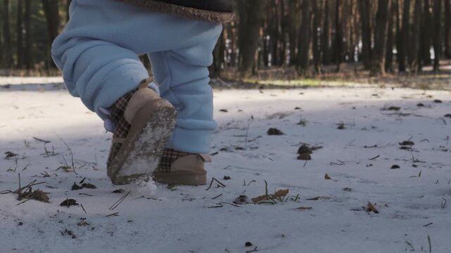 Close up of toddler legs in warm clothes walking unsteadily on snow next to a parent outdoors. Concept of first steps, child development, and family bonding during cold winter days.