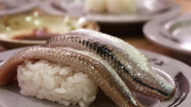 Fresh whole sardine or iwashi nigiri sushi two pieces on ceramic plate with shiny silver skin, Japanese restaurant