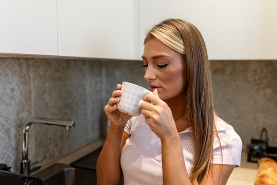 Young woman drinking coffee in kitchen, attractive female holding mug and enjoying hot beverage at home, morning routine and lifestyle concept, person starting day with caffeine in modern house.