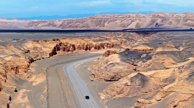Aerial view of a car driving on a winding road through a deep, dramatic canyon in the remote desert of Xinjiang, China.