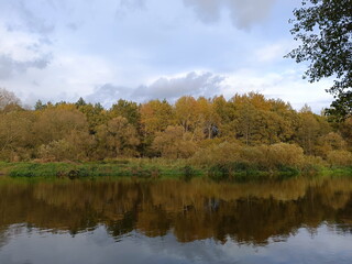 Autumn forest landscape reflected in a river. Scenic fall nature view with cloudy sky