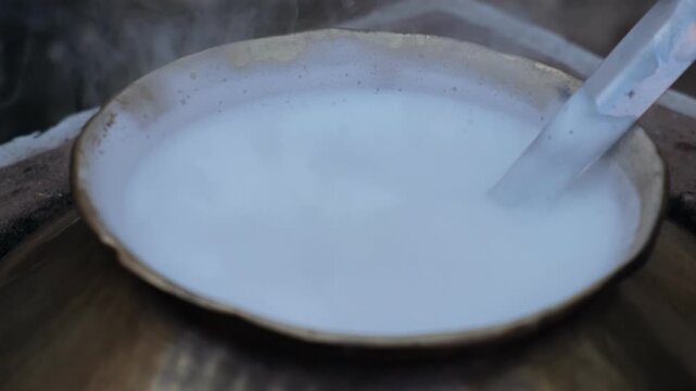 Close-up of fresh milk boiling with foam in a traditional vessel on a rural stove