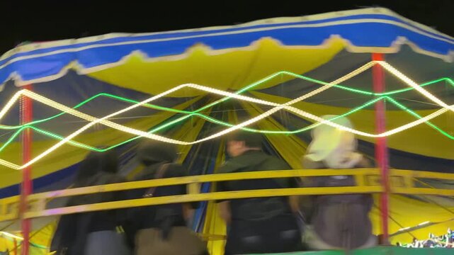 A dynamic Rave Wave amusement ride with bright canopy colors, zigzag LED lights, and thrilling motion, capturing the festive energy of a carnival night
