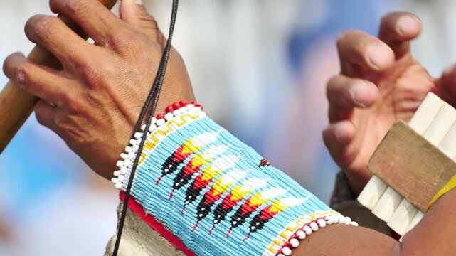 Indigenous musician playing traditional flute instrument with colorful beadwork sleeve