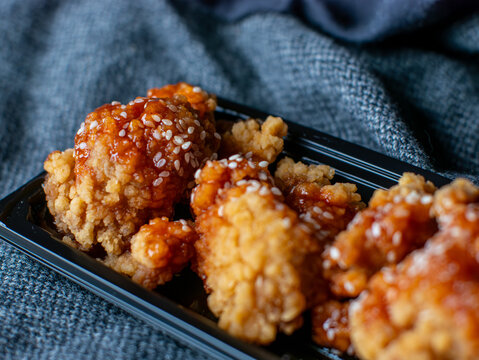 Korean fried chicken with spicy sweet sauce and sesame seeds in black takeout container, yangnyeom chikin delivery