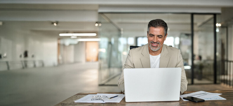 Busy smiling middle aged professional business man executive investor ceo leader using computer working with online finances sitting at desk. Happy mature bank manager looking at laptop in office.