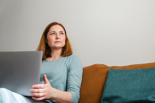 Woman sitting on sofa with laptop, work from home, copy space