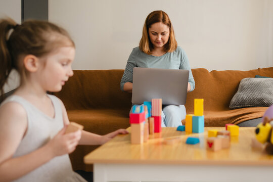 Work from home, mother working at laptop while daughter is playing