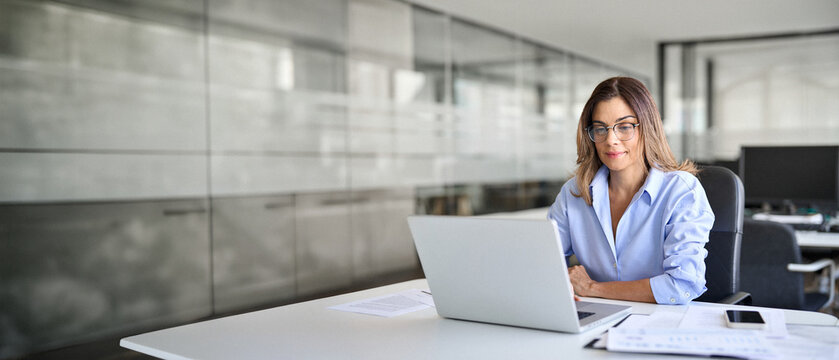 Busy middle aged business woman using laptop working in corporate office. Smiling mature businesswoman executive at work, professional female company hr or bank manager looking at computer.