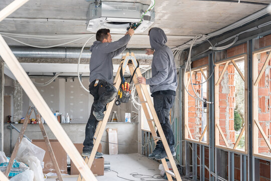 Technicians installing air conditioning unit on construction site