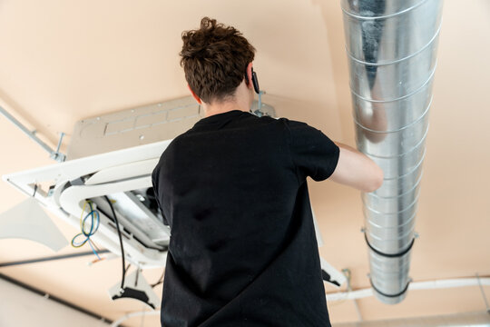 Technician installing air conditioning ceiling unit and ductwork