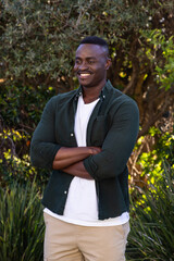 African American man standing arms crossed in garden wearing green shirt beige pants looking right