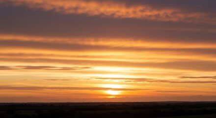 Obraz premium Sunset over a treeline with vibrant orange and yellow streaked clouds