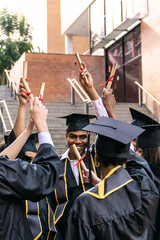 Diverse group of college students in graduation caps and gowns raising their diplomas, celebrating academic achievement and success