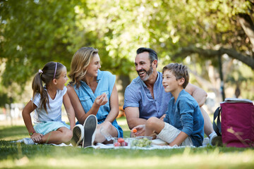 Fototapeta premium Eating, funny and picnic with family in park together for bonding, child development or growth. Food, laughing and parents outdoor on grass field with kids for connection, love or relationship