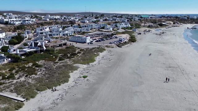 Camera panning up over the beach and town of Paternoster. Paternoster picturesque seaside tourist town with traditional white fishing cottages and houses. 4K Aerial Video.