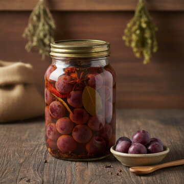 Pickled Governors Plum in Glass Jar with Star Anise and Bay Leaf on Rustic Dark Wooden Table Background