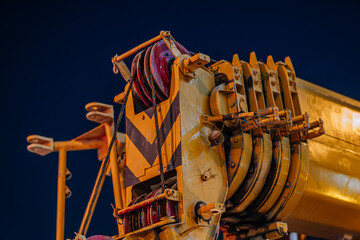 Close-up view of a yellow construction crane's boom with pulleys and cables against a dark night sky backdrop © Raivo