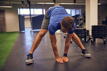 Fototapeta premium Stretching, fitness and health with man in gym for workout, muscle development and flexibility. Exercise, training warm up and wellness with person in sports club for getting ready and challenge
