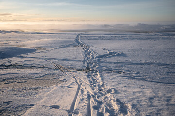 People's steps, ski and sleigh traces on frozen lake surface on cold sunny winter day, place for daily walk and exploring winter season, fishing, skating and having fun in snow, footpath on iced lake.