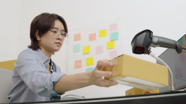 Asian female office worker handle parcel boxes by reading the barcode stickers with a barcode scanner to record the information in the computer.