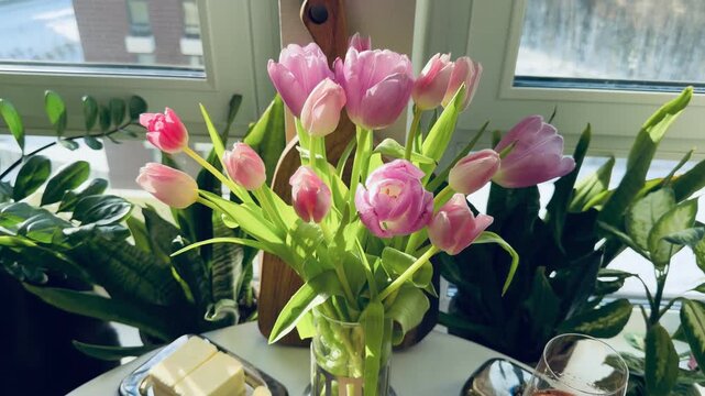 Luxury Maslenitsa breakfast: Russian crepes with black caviar, white wine and pink tulips. Elegant table setting with a black cat among houseplants on the background. Expensive lifestyle concept.