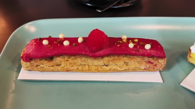 Close-up of an eclair pastry with fruit and cream filling decorated with raspberries on a table in a French cafe.