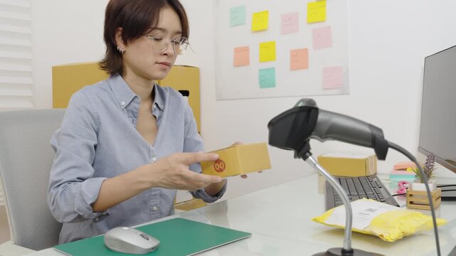 Asian female office worker handle parcel boxes by reading the barcode stickers with a barcode scanner to record the information in the computer.
