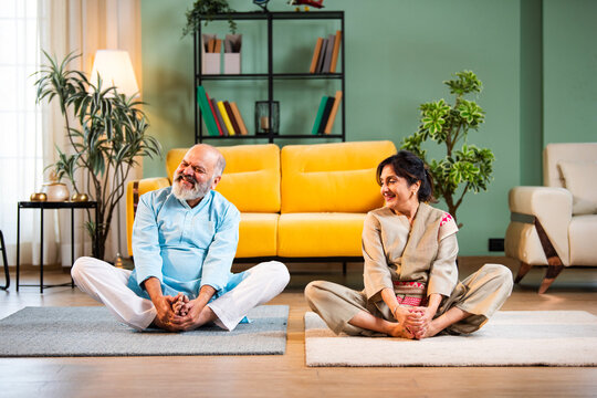 100 charactersIndian senior couple doing stretching doing butterfly warmup or yoga at home in the morning performing sukshma yogic kriya for hip joints while sitting on mat in modern living room