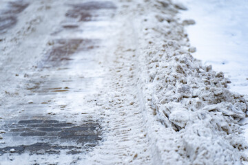 Dirty snow berm along icy roadway with tire tracks and exposed paving stones, close up winter street maintenance scene showing slippery conditions, traction risk and copy space © K