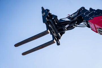 Telescopic handler or boom lift forks in the air, metal pallet forks and hydraulic joints isolated on blue background, industrial transport, load handling © K