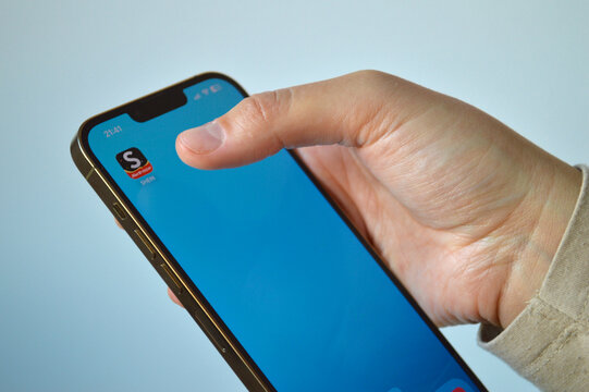 Person using a modern smartphone to browse the Shein shopping app with a Black Friday sale icon on the home screen against a neutral background.