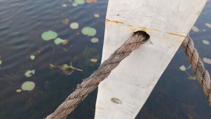 Obraz premium Thick rope passing through a white wooden bridge post over a lake