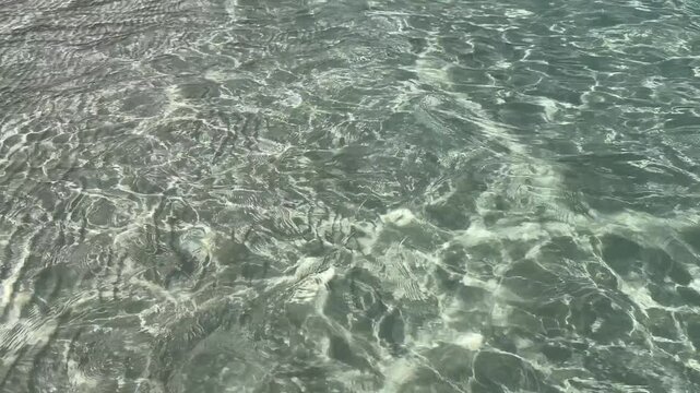 Ultra slow motion view of crystal clear shallow water over white sand about 50 cm deep. Gentle ripples create soft moving light patterns in a calm tropical zen scene.