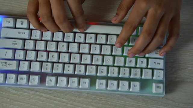 Hands typing on a white compact mechanical keyboard with RGB backlight on a wood desk