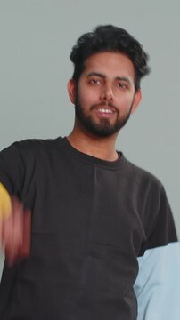 Come here, join us. Welcome. Hindu bearded man showing inviting gesture with hands, ask to join, beckoning to coming, gesturing hello, goodbye. Handsome Indian boy isolated on gray studio background