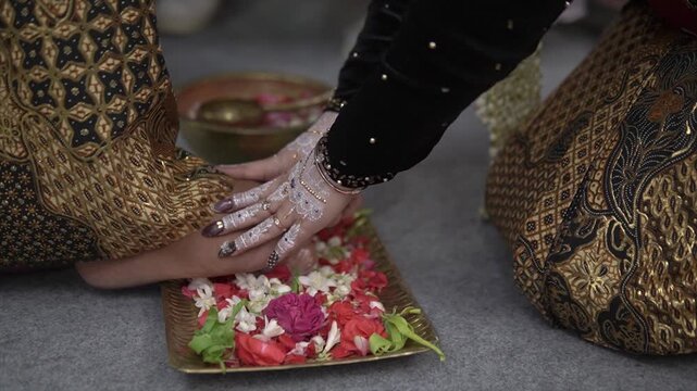 Javanese bride with white henna touching groom's feet during a traditional wedding ritual, 4K.