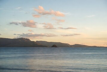 Fototapeta premium Serene Coastal Vista: Tranquil ocean waters meet the silhouette of distant mountains beneath a pastel-hued sky, evoking a sense of calm and natural beauty.