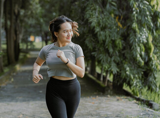 Happy young asian woman wearing sportswear jogging in the park at sunrise. Workout exercise in the morning. Healthy and active lifestyle concept.