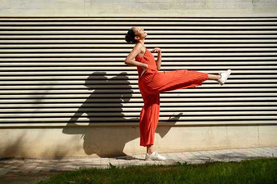 Energetic woman dressed in vibrant scarlet jumpsuit demonstrating perfect high kick outside