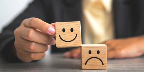 Mental health care concept and training in emotional control with a hand placing a smiling wooden block on top of a sad faced block