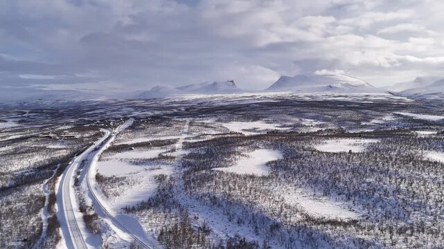 Aerial drone view of snow-covered Lapporten valley in Abisko, Sweden, with a winding winter road through a remote Arctic landscape under cloudy skies