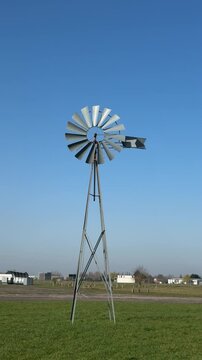 Traditional metal windmill standing in a green field under a clear blue sky