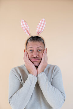 Man with grey hair and brown sweater with Easter bunny ears standing in front of brown background