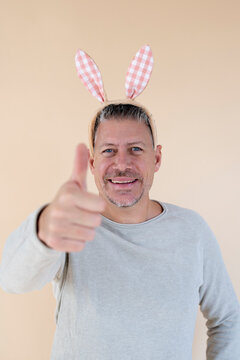 Man with grey hair and brown sweater with Easter bunny ears standing in front of brown background