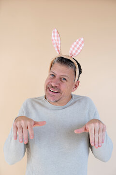 Man with grey hair and brown sweater with Easter bunny ears standing in front of brown background